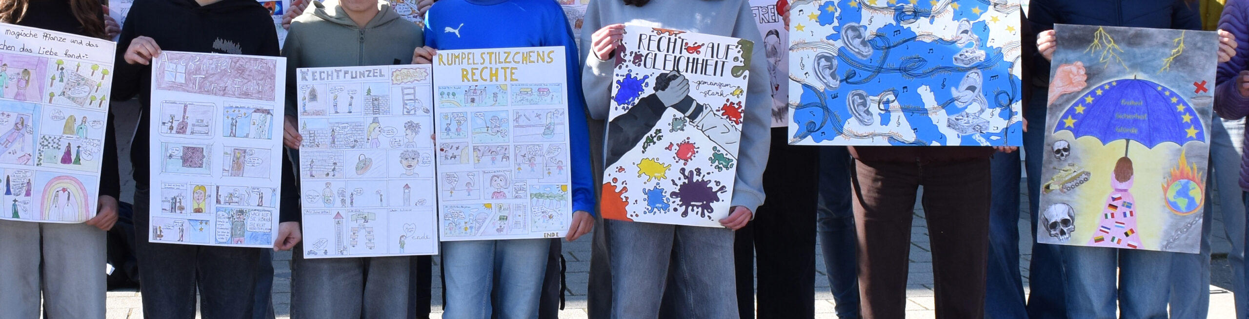 Schüler halten ihre Plakate vor sich, die sie gestaltet haben